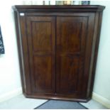 A late 19thC oak hanging corner cupboard with canted flanks, enclosed by a pair of lockable,