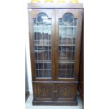 An early 20thC Arts & Crafts inspired oak display cabinet with two lead glazed doors,