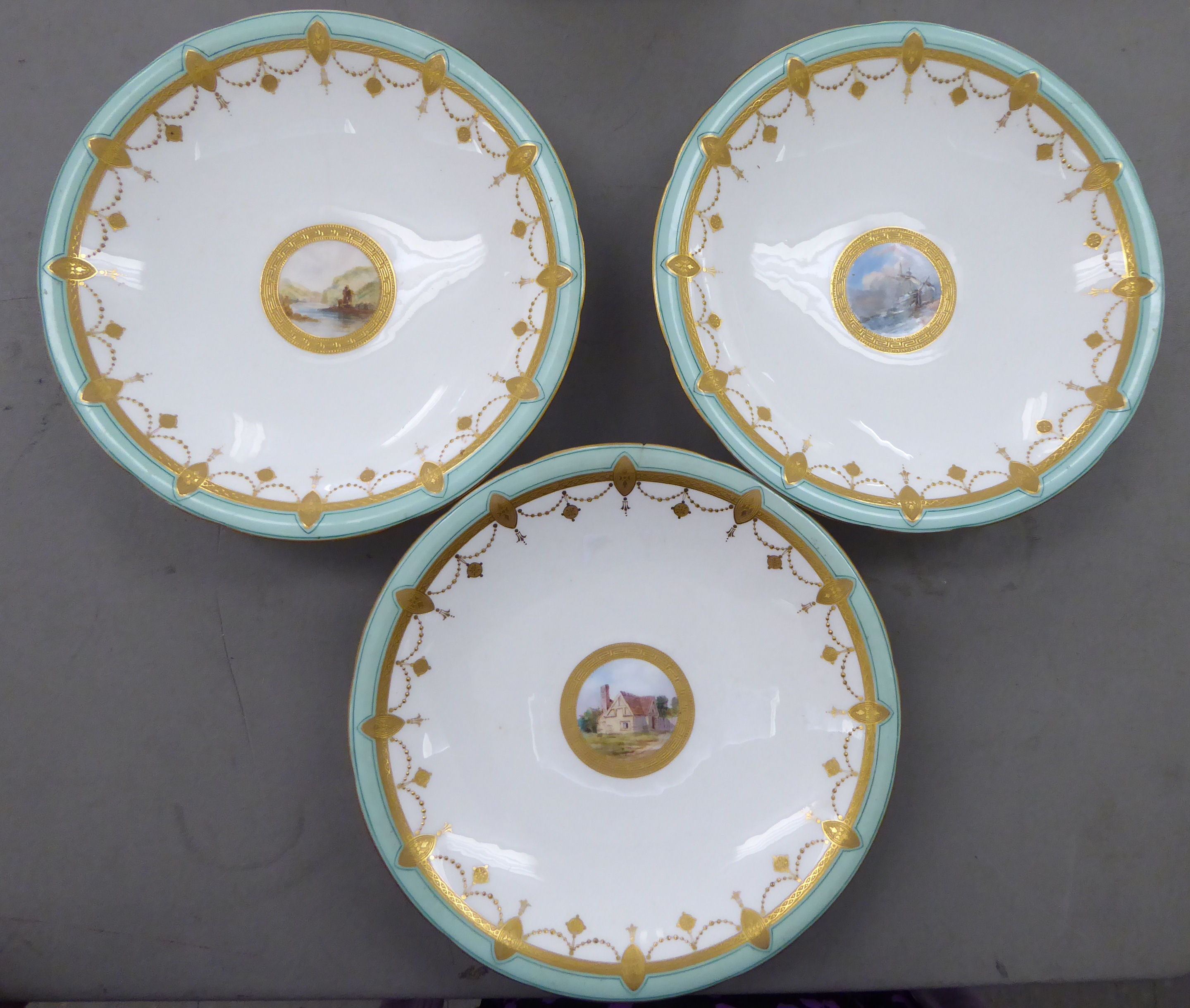 An early 20thC Minton porcelain dessert service, decorated with landscapes, cartouches,