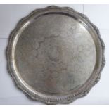 An Iraqi silver coloured metal tray, having a raised, wavy edge, cast,