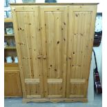 A modern honey coloured pine triple wardrobe, enclosed by three fielded, panelled doors,