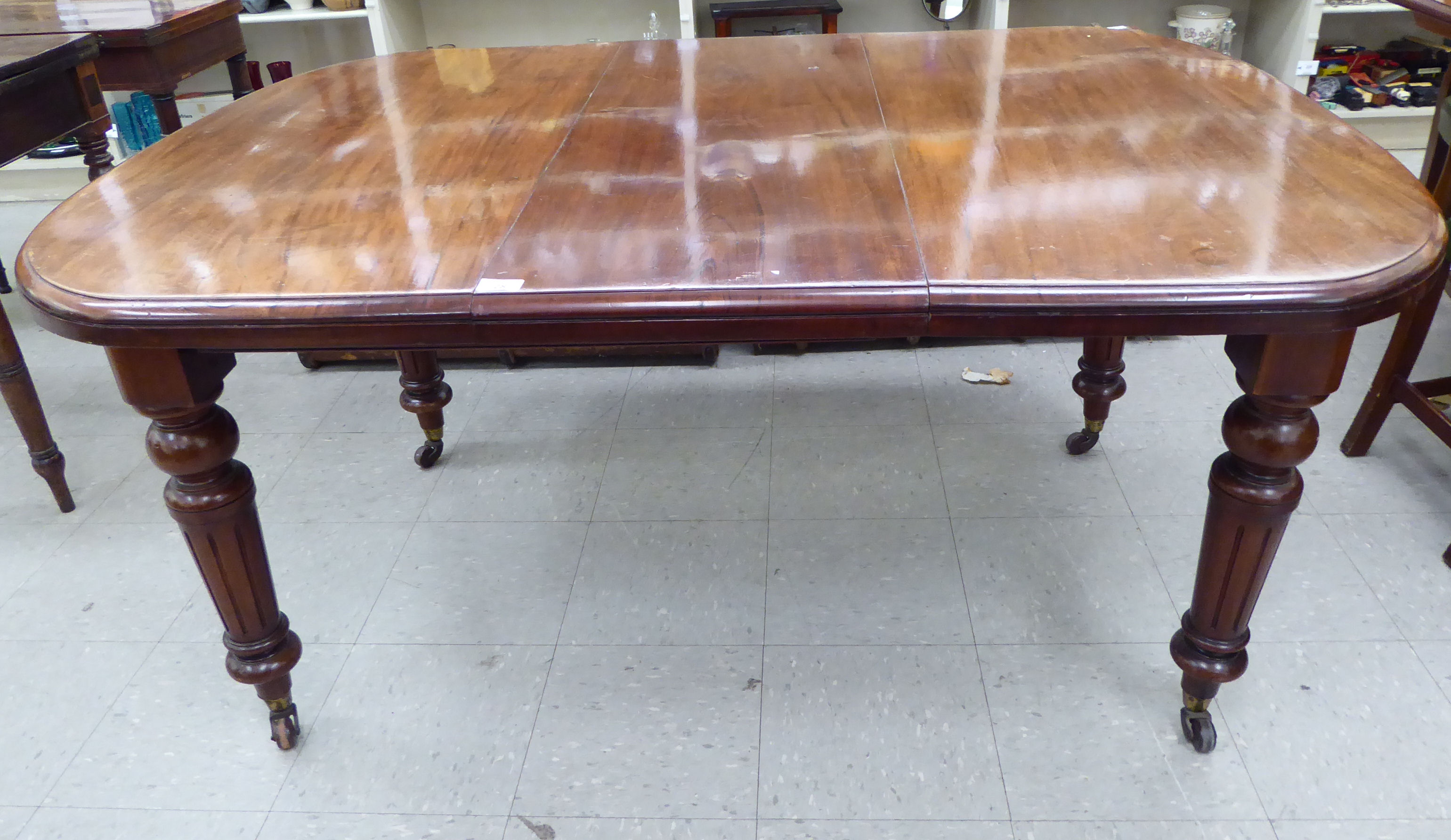 A late Victorian mahogany wind-out dining table, the top with a curved edge, raised on tapered,