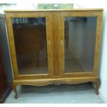 A mid 20thC walnut veneered display cabinet with two glazed doors,