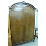 A mid 20thC walnut wardrobe with an arched top and a pair of panelled doors,