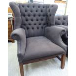 A mid 20thC wingback armchair, part button upholstered in dark brown fabric,