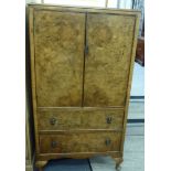 A mid 20thC burr walnut and mahogany finished cupboard with a pair of doors, over two drawers,