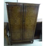 An early/mid 20thC burr walnut finished cupboard with a pair of doors, raised on stubby,