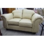A modern cream coloured hide two person settee with showwood framed arms and cream coloured crushed