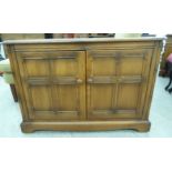 An Ercol light coloured elm base cabinet, comprising two panelled doors,
