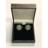 A pair of white metal set flower cluster earrings, the petals set with diamonds, with emeralds to