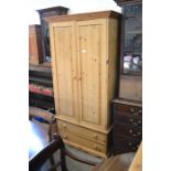 A small stained pine wardrobe with panelled doors enclosing a hanging rail over two long drawers