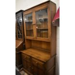 Two similar Ercol elm display cabinets with glazed doors, panelled cupboards and drawers