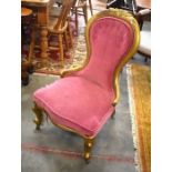 A gilt painted Victorian mahogany nursing chair with pink upholstery, cabriole supports and castors