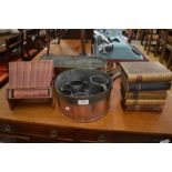 A small wooden book trough holding a set of red leather bound reference books, a copper fish