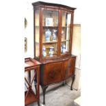 A mahogany serpentine front display cabinet with glazed doors over panelled cupboard doors raised on