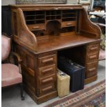 A large oak roll top desk, the sliding tambour panel enclosing a fitted interior over six drawers