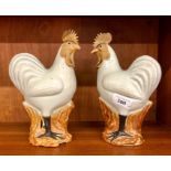 A pair of Chinese Export style figures of cockerels or hens; each bird perched on rockwork, post