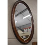 An oval bevelled edge mirror in beaded oak frame
