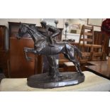 A bronzed figure of a steeplechase horse and jockey taking a jump