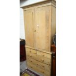 An antique stripped pine linen press, the pair of panelled doors enclosing fitted slides over two