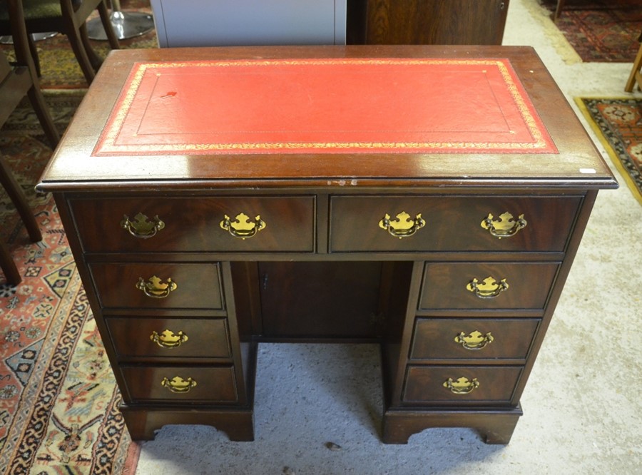 A mahogany kneehole desk with gilt tooled red leather top over eight drawers and central niche