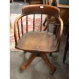 An early 20th century spindle back swivel desk chair with shaped saddle seat and quadraform supports