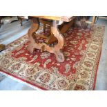 A Pakistan made Farhan wool rug with scrolling floral design on red ground within palmette border