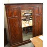 A large mahogany triple combination wardrobe, the central mirrored door enclosing slides and drawers