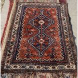 A Persian Shiraz rug with a double linked navy medallion on red ground, ivory border decorated