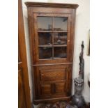 A floor standing oak corner cabinet with glazed door over panelled cupboard raised on shaped bracket