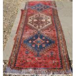 An antique worn Persian Hamadan runner with three central geometric medallions on rust ground within