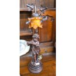 An Art Nouveau style figural table lamp of a child holding a flute with amber glass shade above