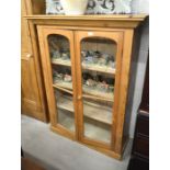 A stained pine display cabinet with a pair of glazed doors enclosing three shelves