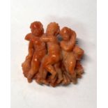 A Victorian or earlier carved coral brooch featuring cherubic Three Graces in high relief, with