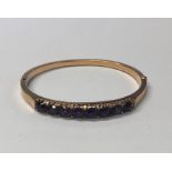 An Edwardian yellow metal half hinged oval bangle set with eight claw-set circular amethysts with