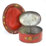 An oval Tole ware box and cover on stand, painted with flowers on a red ground, 22 cm wide to/w a
