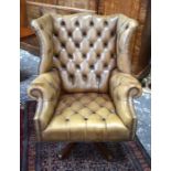 A tan leather button upholstered wingback swivel chair