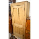 A stripped pine hall cupboard with a full length quad panelled door enclosing an open  hanging space