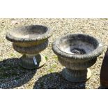 A pair of Georgian style weathered garden urns on pedestal  bases