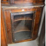 An antique stained pine hanging corner cupboard with a single glazed door enclosing two shelves