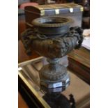 A cast iron classical urn decorated with face masks
