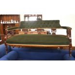 An Edwardian carved mahogany salon settee with green button back upholstery raised on turned