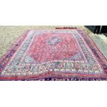 A Persian Mashad carpet, traditional floral design on rose ground centred by a navy floral