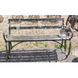 A weathered slatted teak garden bench with green painted scrolling iron supports