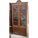 A carved oak bookcase with a pair of leaded doors and panelled cupboard doors raised on a plinth