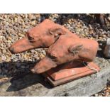 A cast composite terracotta garden sculpture of two greyhound heads mounted on rectangular base