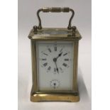 A small early 20th century lacquered brass carriage alarm clock