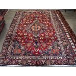 A Persian Mashad small carpet, traditional floral design on red ground within a navy palmette border