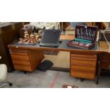 A large teak office desk with tooled dark leather top, fitted with slides and drawers