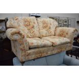 A two seater scroll arm sofa with floral upholstery, turned front supports with brass castors